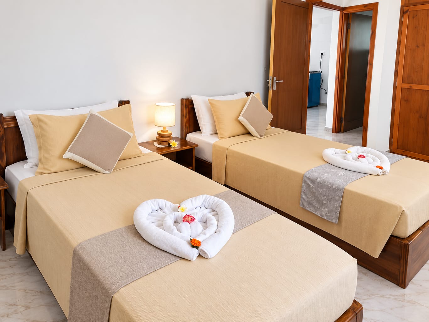 The One-Bedroom House bedroom: two single beds with beige covers and decoratively folded towels, with a lamp on the bedside table between them.
