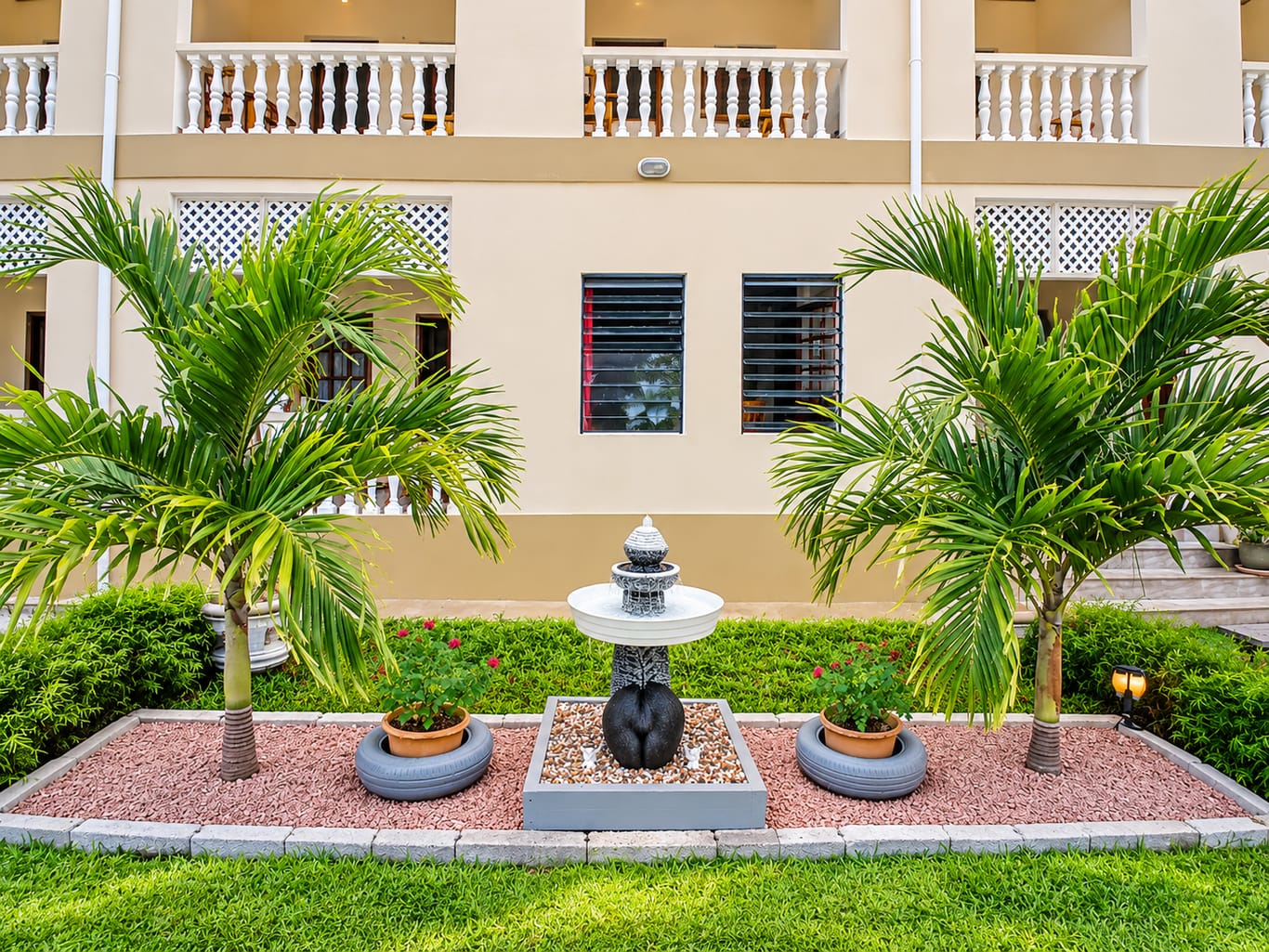 The guesthouse garden: palms either side of a small fountain, in front of the cream walls and white-balustraded balconies.